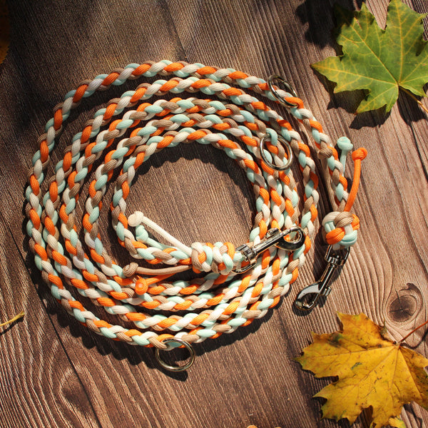 Paracord-Hundeleine Ljus in Orange, aufgerollt auf Holz, mit Karabinern und Ringen.